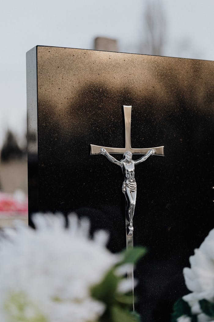 A detailed silver crucifix on a reflective black background with soft floral foreground.