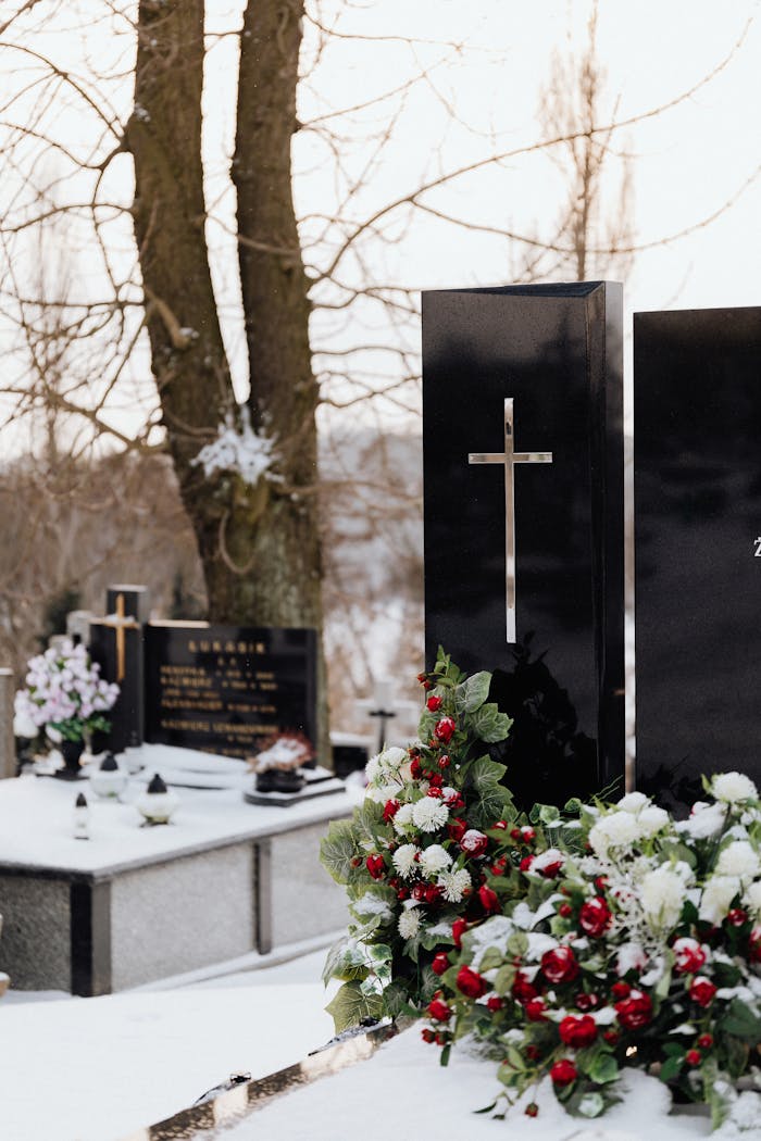 Serene cemetery view with snow and floral arrangements in winter.