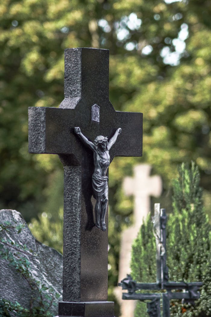Marble cross with Jesus in a peaceful cemetery setting.